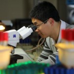 Xi Wu looks through a microscope in a science lab